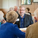 A man is seated at a table looking at other people at the table